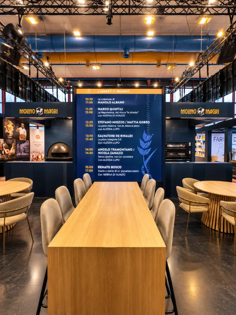 Stand espositivo Molino Magri con tavoli e palinsesto.webp
