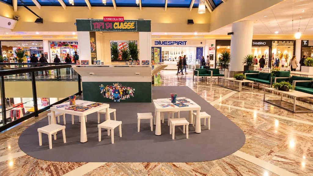Area bimbi con edicola colorata al centro commerciale.webp